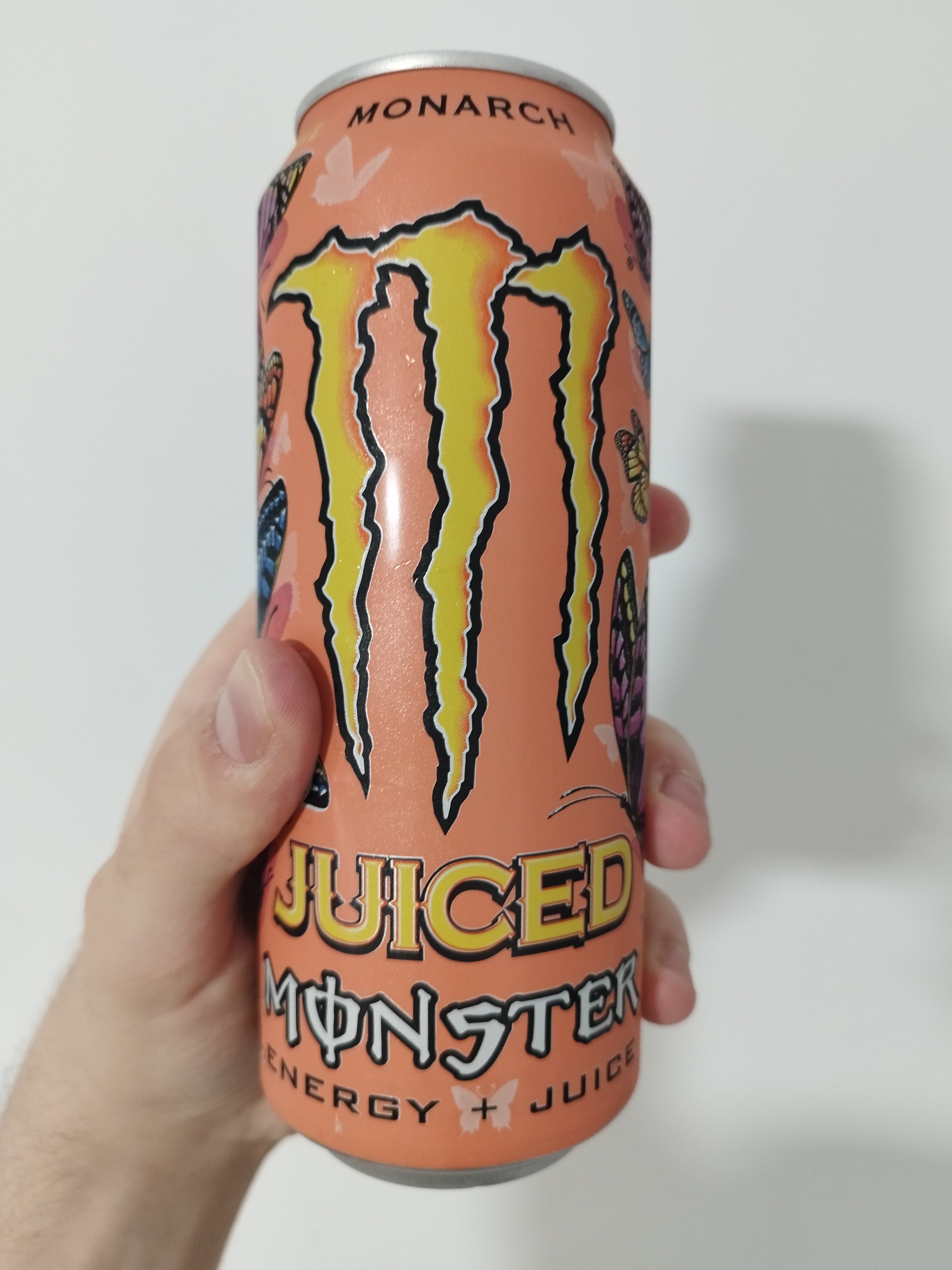 a peach-coloured can of juiced monster monarch. there are butterfly drawings around the logo.